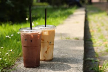 Dışarıdaki yeşil çimlerin yanında soğuk kahve bardakları ile paket plastik bardaklar, mesaj için yer.