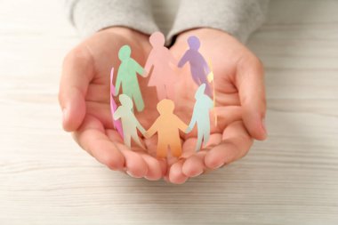 Man holding paper human figures at white wooden table, closeup. Diversity and inclusion concept