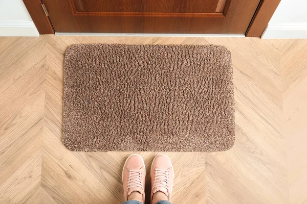 Woman standing near door mat on wooden floor in hall, top view