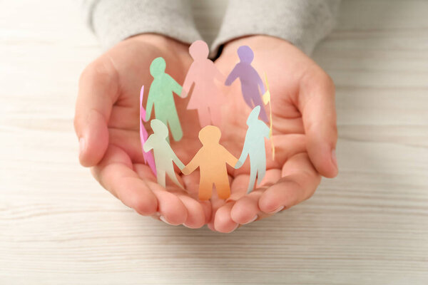 Человек держит бумажные человеческие фигуры за белым деревянным столом, крупным планом. Концепция разнообразия и интеграции