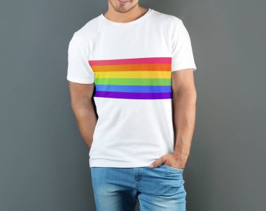 Gri arkaplanda LGBT gurur bayrağı resmi olan beyaz tişört giyen genç adam