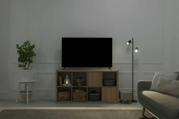 Modern TV on cabinet, sofa and beautiful houseplants indoors. Interior design