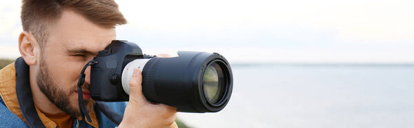 Male photographer taking picture with professional camera outdoors, space for text. Banner design