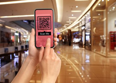Woman holding smartphone with QR code on screen in shopping mall, closeup
