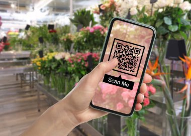 Woman holding smartphone with QR code on screen in flower shop, closeup