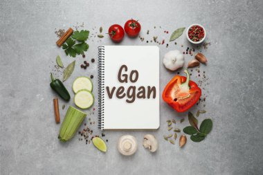 Deyimli defter Go Vegan, taze sebze ve baharatlar açık gri arka planda, düz yatıyordu