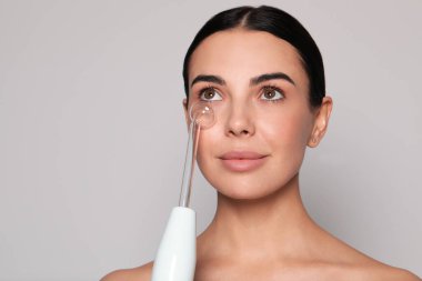 Gri arka planda yüksek frekanslı darsonval cihaz kullanan bir kadın. Metin için boşluk