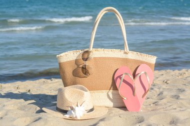 Güneşli bir günde deniz kenarında şık bir çanta ve diğer plaj aksesuarları.