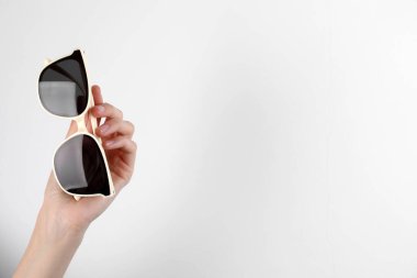 Beyaz arka planda şık güneş gözlüğü tutan kadın, yakın plan. Metin için boşluk