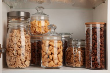 Rafta farklı kahvaltı gevrekleri olan cam kaplar.