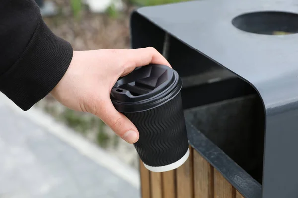 Man throwing black paper cup into trash can outdoors, closeup