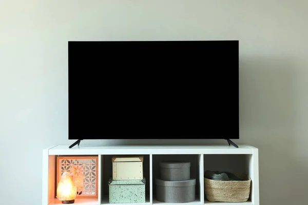Modern TV and lamp on cabinet near white wall indoors. Interior design