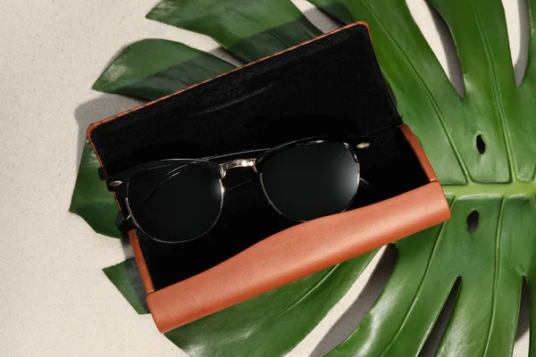 Stylish Sunglasses Brown Leather Case Tropical Leaf Sand Flat Lay — Stockfoto