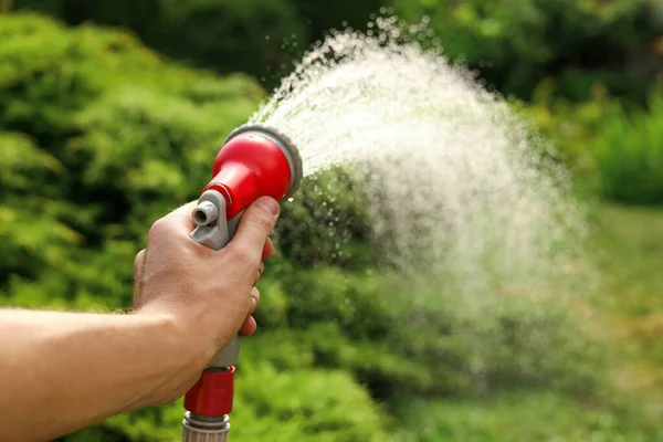 Man spraying water from hose in garden, closeup