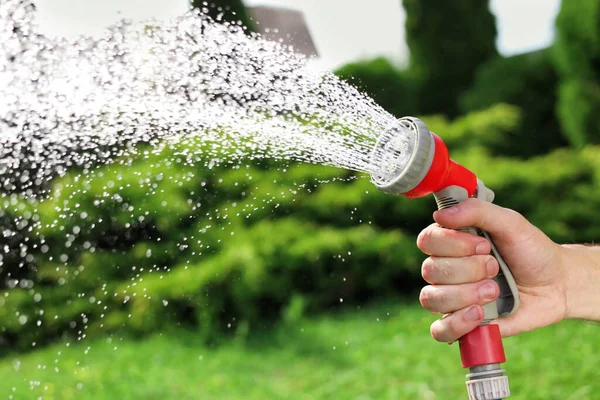 Man spraying water from hose in garden, closeup