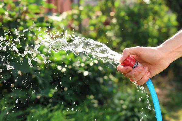 Man pouring water from hose in garden, closeup