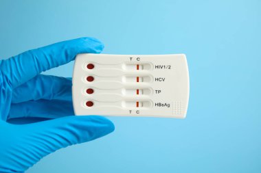 Doctor holding disposable express test for hepatitis on light blue background, closeup