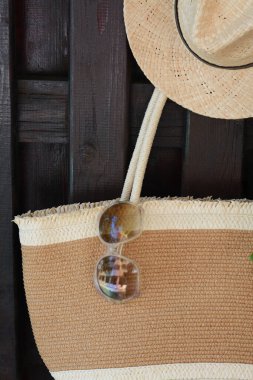 Dışarıdaki ahşap çitlerde asılı duran şapkalı ve güneş gözlüklü şık bir çanta. Plaj aksesuarları