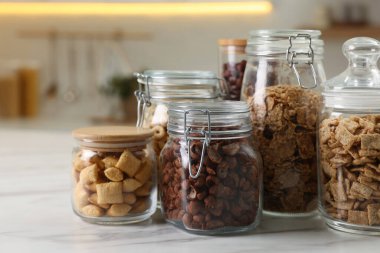 Glass containers with different breakfast cereals on white marble table in kitchen
