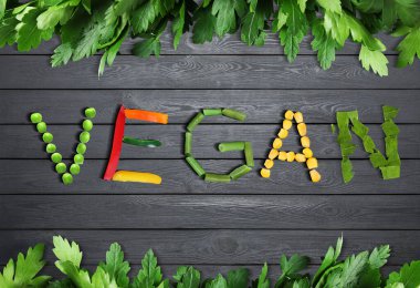 VEGAN, gri ahşap arka planda farklı taze sebzelerden yapılmıştır.