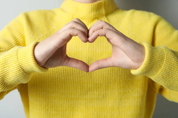 Woman making heart with her hands on light grey background, closeup