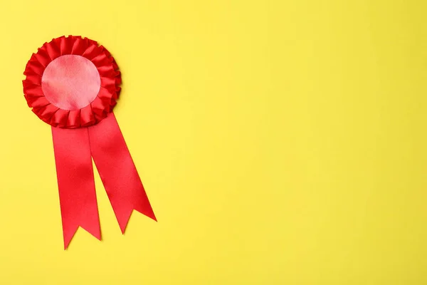 Red award ribbon on yellow background, top view. Space for text