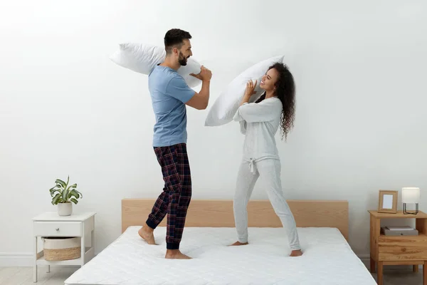 Happy couple having pillow fight on bed with comfortable mattress at home