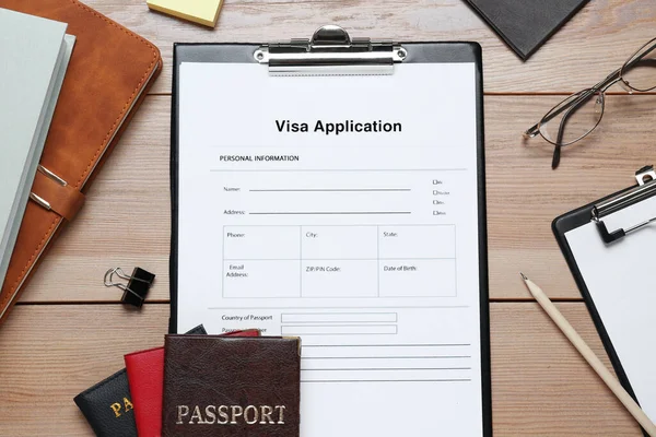 Visa application form for immigration, passports and stationery on wooden table, flat lay