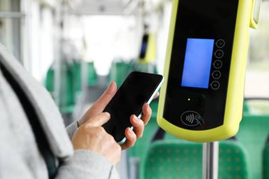 Akıllı telefonu olan kadın toplu taşımacılıkta ulaşılamaz ücret ödeme cihazının yakınında, yakın plan.