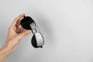 Woman holding stylish sunglasses on light background, closeup. Space for text