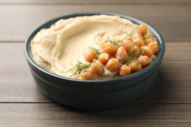 Bir kase lezzetli humus, nohut ve dereotlu ahşap masa, yakın plan.