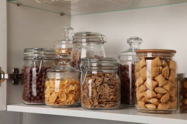 Rafta farklı kahvaltı gevrekleri olan cam kaplar.