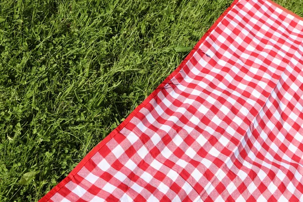 Checkered picnic tablecloth on fresh green grass, closeup. Space for text