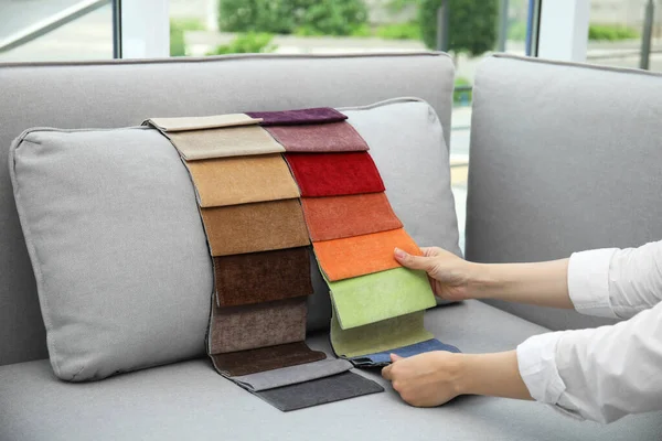 Woman choosing fabric among colorful samples on grey sofa at home, closeup