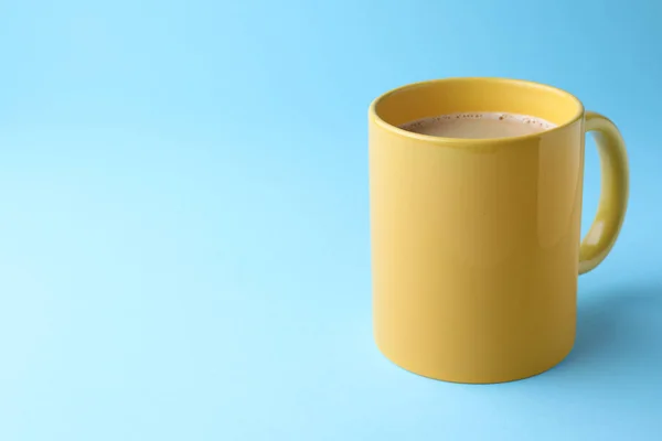 Yellow mug of freshly brewed hot coffee on light blue background, space for text