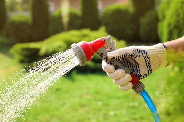 Man spraying water from hose in garden, closeup