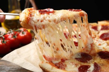 Ahşap masada lezzetli biberli pizza yiyen bir kadın, yakın plan.
