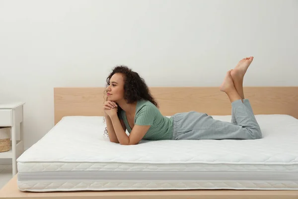 Happy young African American woman on bed with comfortable mattress at home