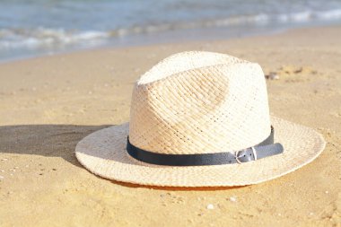Stylish straw hat on sandy beach near sea