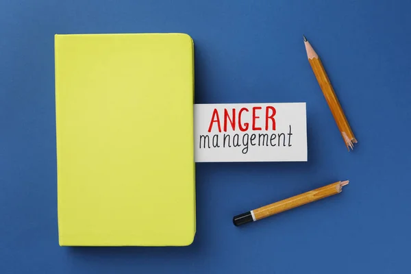 Card with words Anger Management, notebook and broken pencil on blue background, flat lay