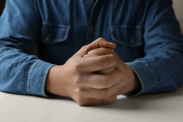 Man clenching hands at table while restraining anger, closeup