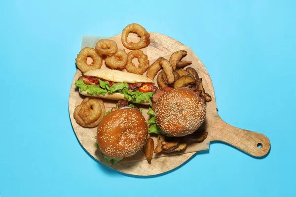 Tasty burgers, hot dog, potato wedges and fried onion rings on light blue background, top view. Fast food