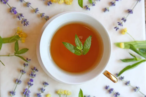 Tasty herbal tea and flowers on white table, flat lay