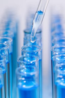 Test tüpüne ışık arka planında mavi sıvı damlatılıyor, yakın plan. Laboratuvar analizi