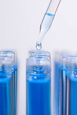 Test tüpüne ışık arka planında mavi sıvı damlatılıyor, yakın plan. Laboratuvar analizi