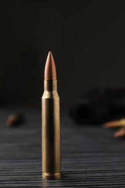 Bullet on black wooden table, closeup. Military ammunition