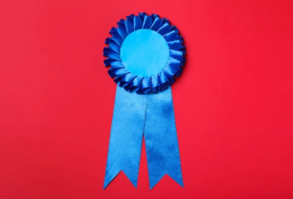 Blue award ribbon on red background, top view