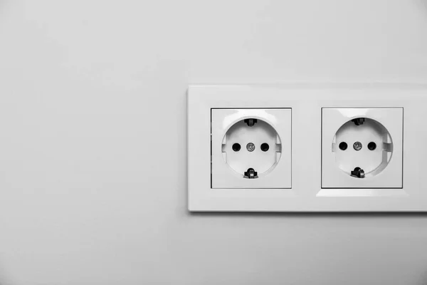 Power sockets on white wall, space for text. Electrical supply