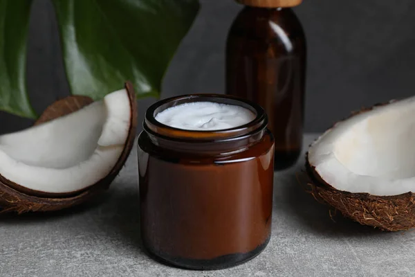 Jar of hand cream and coconut pieces on grey table