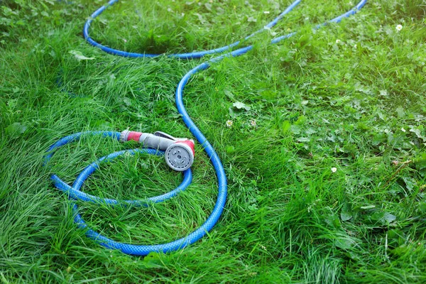 Watering hose with sprinkler on green grass outdoors, space for text